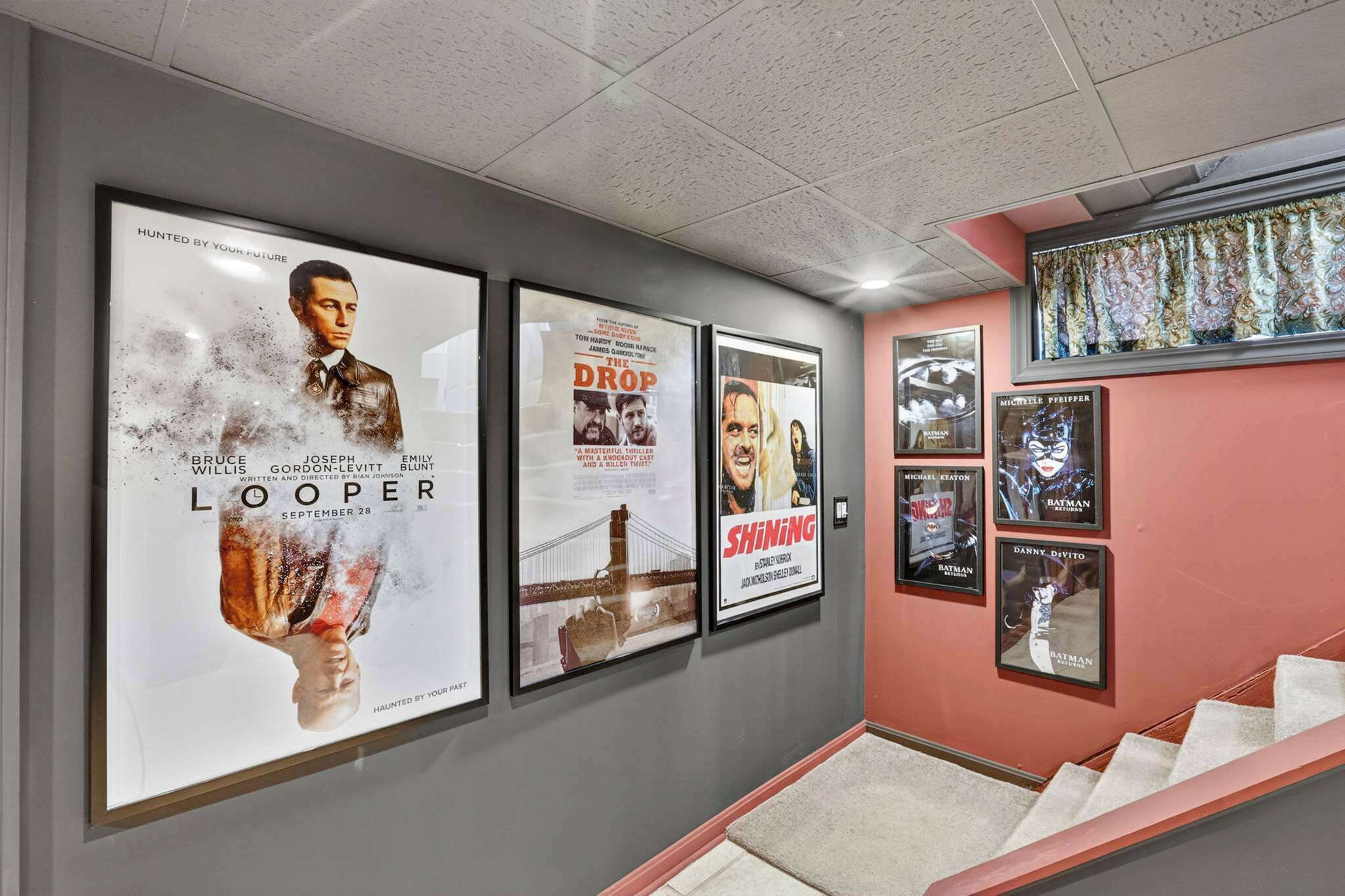 A hallway with framed movie posters on the wall, a staircase, and a window with patterned curtains.
