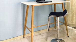 Pieni, moderni huone, jossa on valkoinen työpöytä, kannettava tietokone, musta tuoli ja verho.