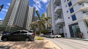A high-rise residential building with multiple balconies, a 7-Eleven store, and parked cars on the street. - The City Escape: Stylish Condo Near Ayala Bloc & IT Park (Cebu City)
