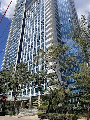 Ein Hochhaus mit moderner Glasfassade, mehreren Balkonen und einem begrünten Eingangsbereich.