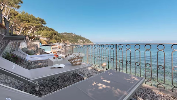 Una terraza frente al mar con sillones, una mesa y barandilla metálica.