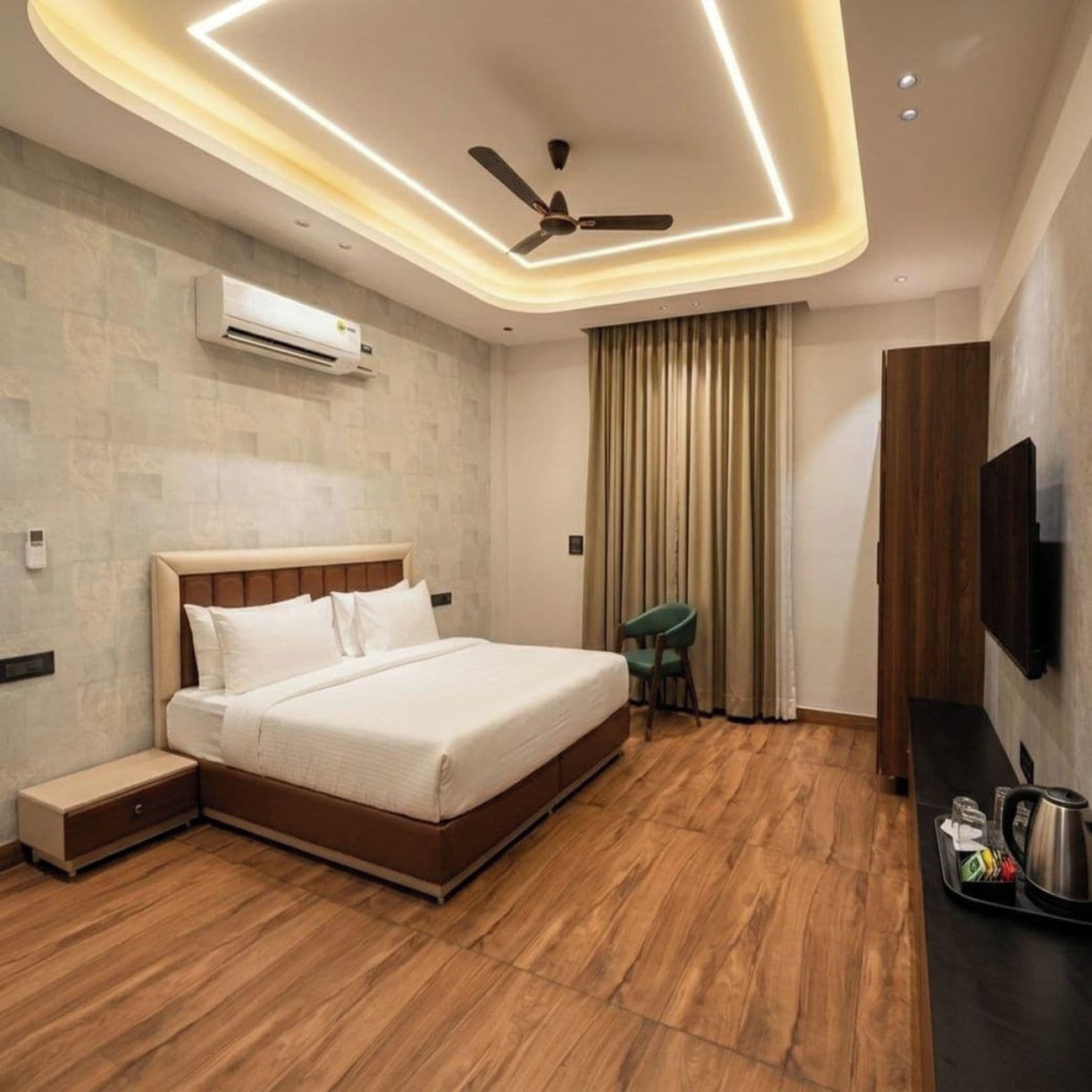 A modern hotel room with a bed, a desk, a chair, an air conditioning unit, a ceiling fan, and a flat-screen TV.