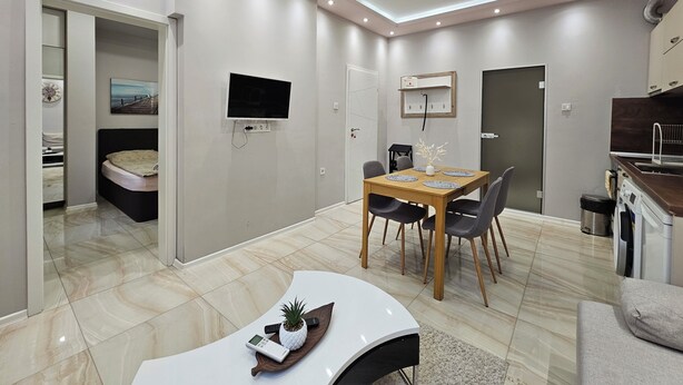 A modern apartment with a dining area, a TV mounted on the wall, a kitchen with a sink, and a bed in the adjacent room. - Quality&Design
Vitosha Blvd (Sofia)