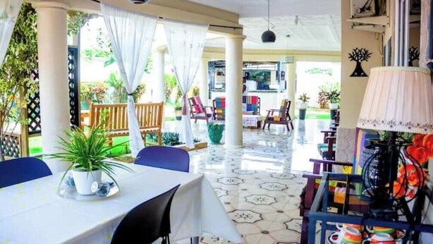Un espace extérieur abrité, aménagé pour les repas, avec des tables, des chaises et des plantes en pot.