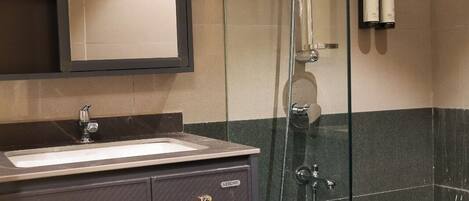 A bathroom with a glass shower enclosure, a sink, and a mirror.