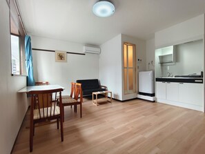 A compact living space with a dining table, two chairs, a sofa, a small table, a kitchen area with a refrigerator, and a window with a curtain. - 9 minutes from JR Namba Station/Airport Bus Terminal, 6 minutes from JR Ashiwarabashi Station, close to both Shinsaibashi and Kyocera Dome Osaka. 403 Ohara (大阪市浪速区塩草３丁目)