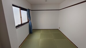 Ein Zimmer mit Tatami-Bodenbelag, einem Fenster mit Vorhang und einer Deckenleuchte.