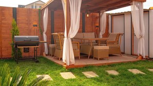 Un espacio de estar al aire libre cubierto con mobiliario de mimbre, una parrilla y una pérgola con cortinas.