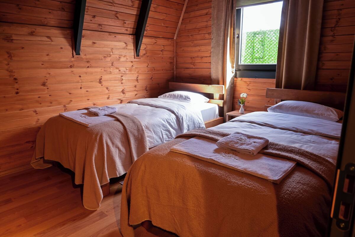 A cabin with two wooden beds, a window with curtains, and a wooden floor.
