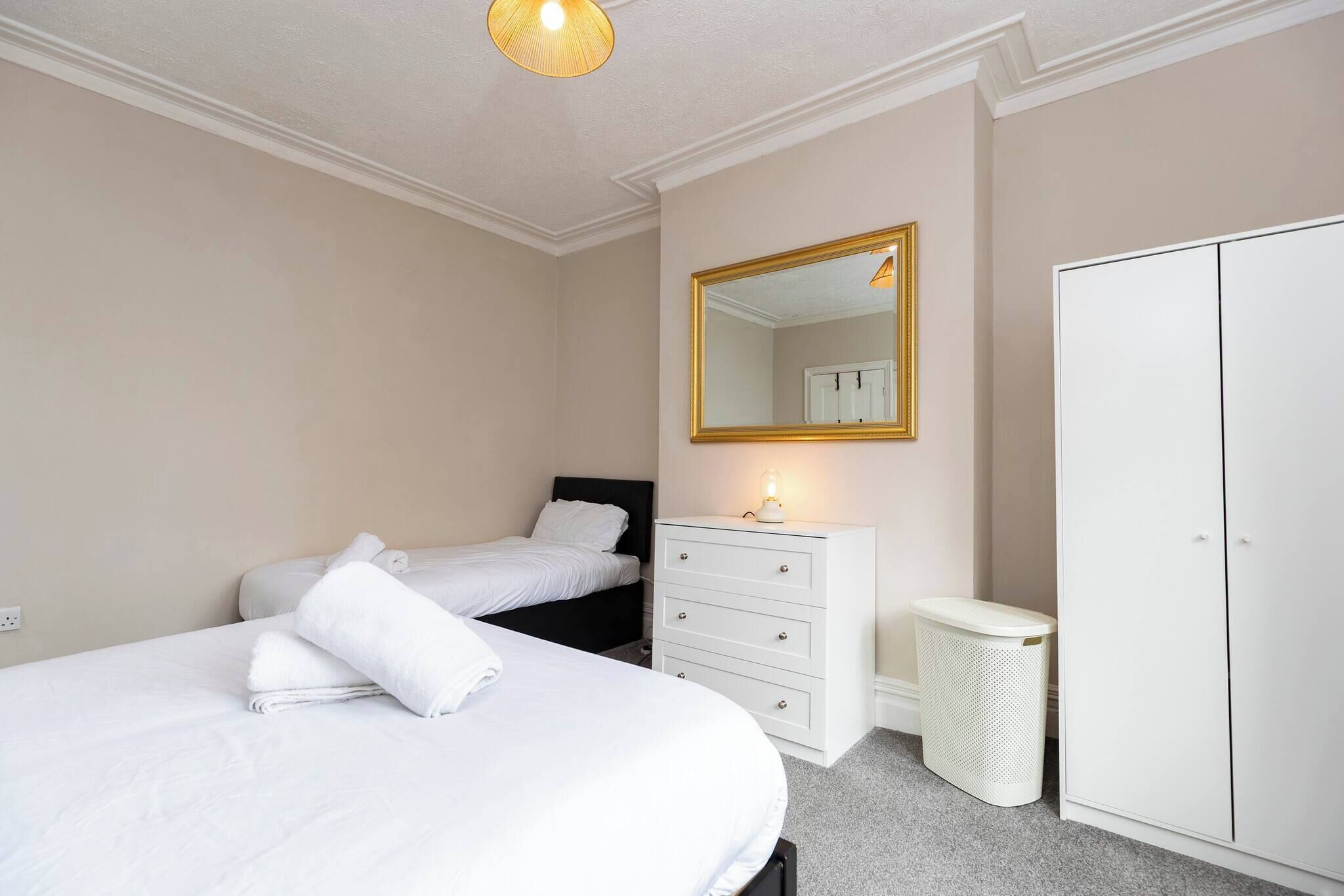 A bedroom with two beds, a dresser, a mirror, a wardrobe, and a trash bin.