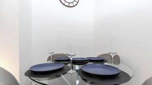 A round glass table with blue plates and wine glasses, set against a white wall with a clock. - Cosy Home 7 Minutes From Newcastle City Centre (Gateshead)