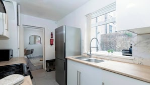 A compact kitchen with a refrigerator, sink, and window overlooking a brick wall. - Cosy Home 7 Minutes From Newcastle City Centre (Gateshead)