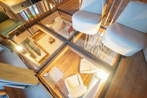 A high-ceilinged room with a glass floor, a sofa, two chairs, and a wooden floor.