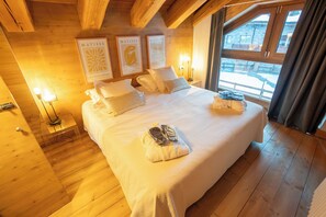 A wooden-paneled room with a large bed, two wall-mounted lamps, and framed artwork.