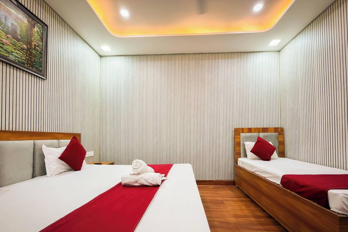 A hotel room with two beds, a wooden headboard, a red throw blanket, and a painting on the wall.