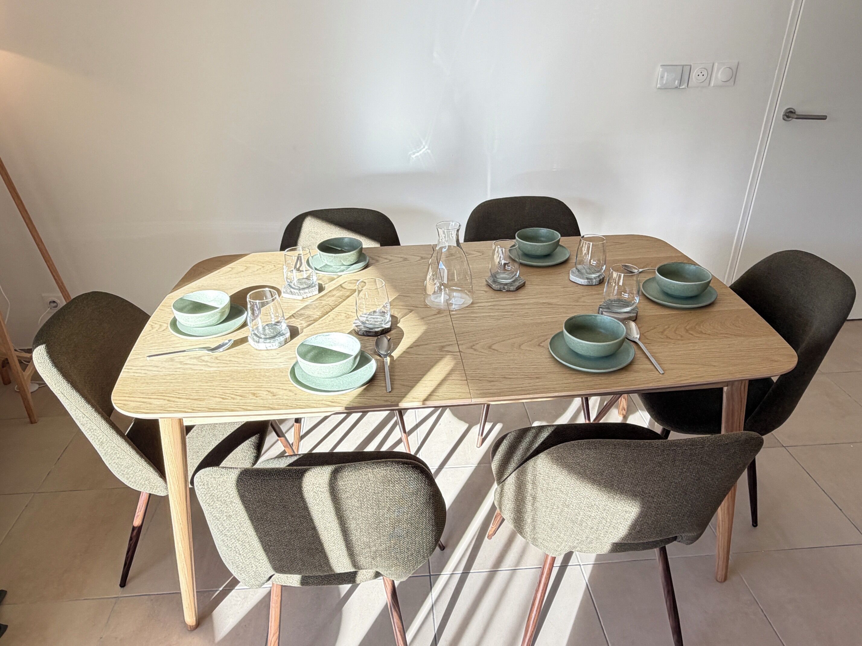 A dining table set with green bowls, glasses, and cutlery, surrounded by chairs.