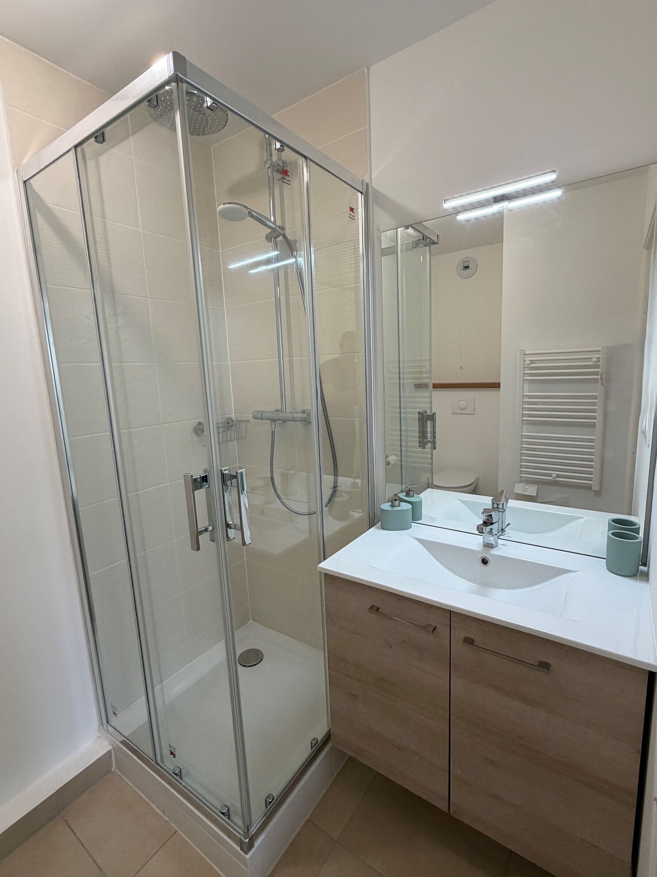 A modern bathroom with a glass-enclosed shower, a white sink with two cups, and a mirror above the sink.
