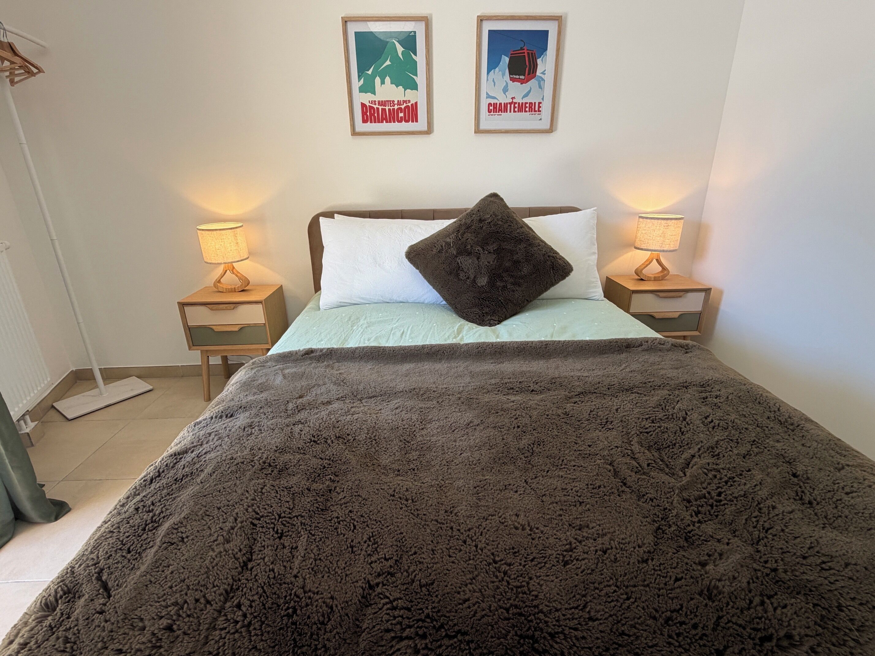 Un letto con una coperta soffice e un cuscino, due lampade sui comodini e due quadri appesi al muro.