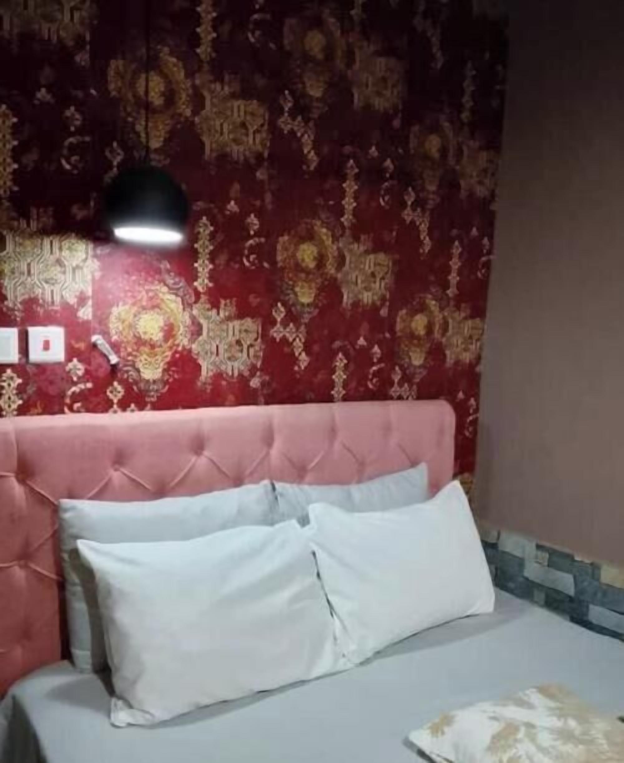A bedroom with a tufted headboard, a bed with white bedding, and a patterned wall.