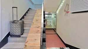 Um corredor de hotel com escada de madeira, mala e sapateira.
