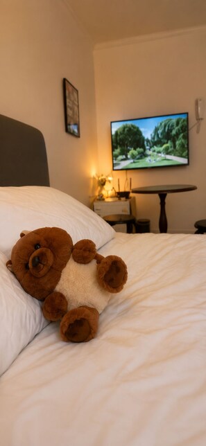 Ein Bett mit einem Teddybär, einem Fernseher an der Wand und einem kleinen Tisch mit einer Lampe.