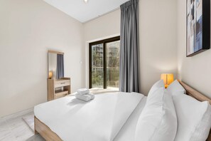 Ein Hotelzimmer mit Bett, Nachttisch, Spiegel, Fenster mit Vorhängen und einem Bild an der Wand.