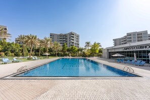 Ein Schwimmbecken mit Liegestühlen, Palmen und einem Gebäude mit der Aufschrift 'MAG5 CLUBHOUSE'.