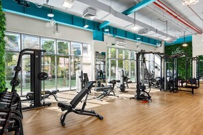 Ein Fitnessstudio mit unterschiedlichen Trainingsgeräten, großen Fenstern und einer grünen Wand.