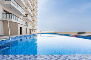 Ein Schwimmbecken mit blauen Mosaikfliesen, einem Rettungsring und einem Balkon mit Blick auf ein Gewässer.