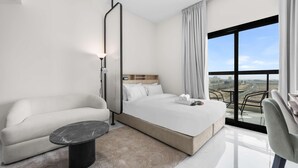 A modern hotel room with a bed, a sofa, a small table, and a balcony with a view. - Free Housekeeping Visits During Your Stay - Stayshort - Peaceful Studio in Jebel Ali That Sleeps 2 (Dubai)