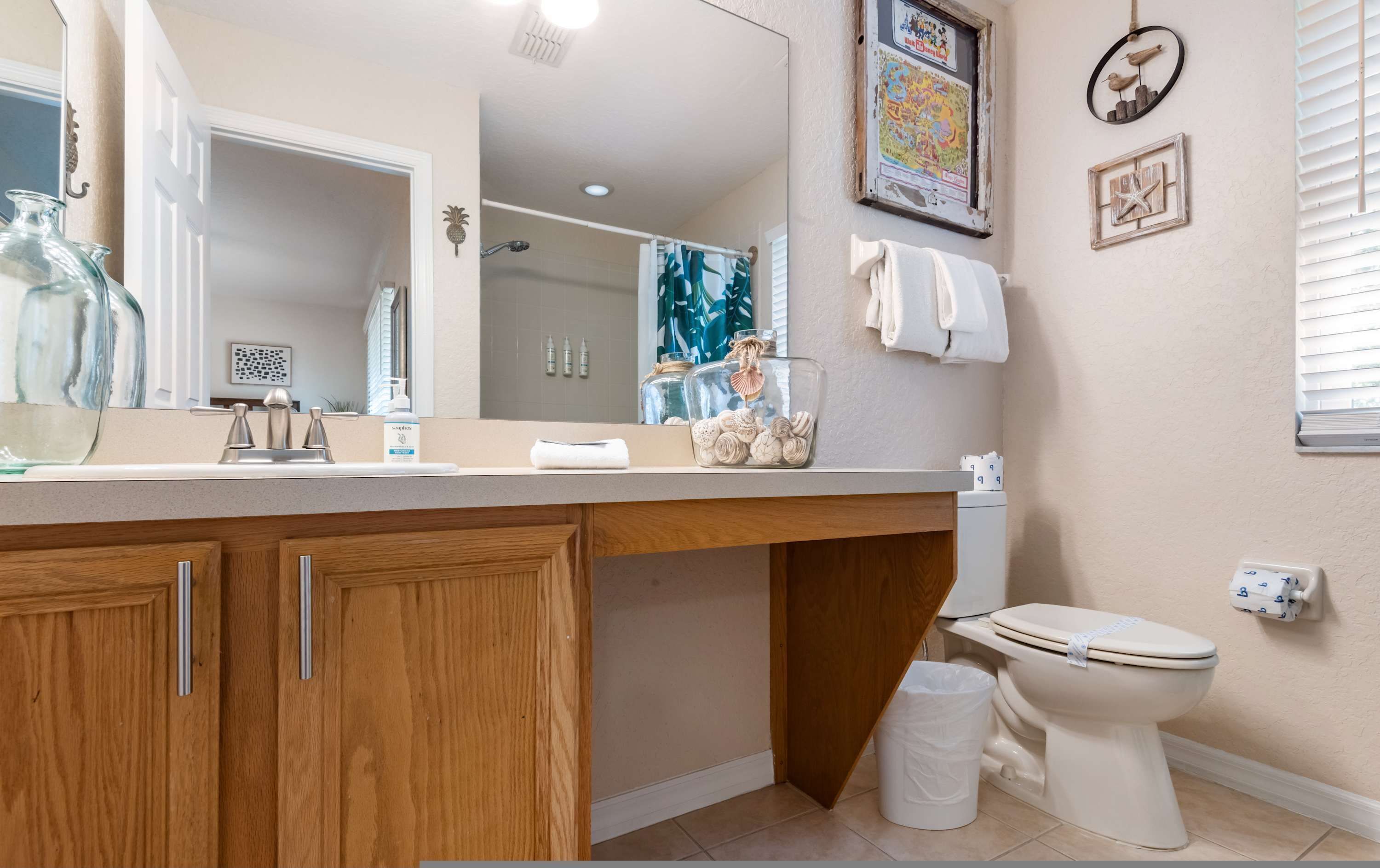 A bathroom with a wooden vanity, a toilet, a trash can, and a mirror.