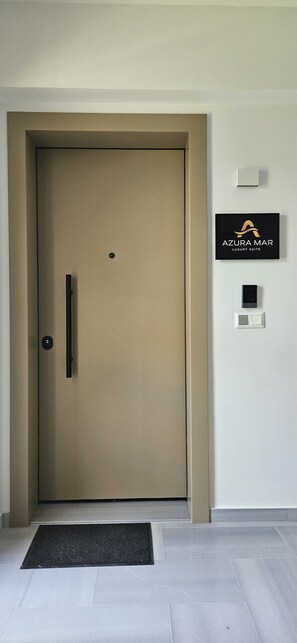 Eine geschlossene Tür mit Griff, eine schwarze Fußmatte und ein Schild an der Wand mit der Aufschrift 'AZURA MAR LUXURY SUITE'.