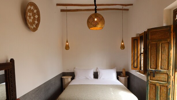 A bedroom with a bed, wooden beams, hanging pendant lights, a decorative wall plate, and a wooden wardrobe. - New Luxurious Boutique Riad 4bdr Private house (Marrakech)