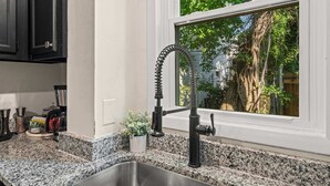 A kitchen with granite countertops, a stainless steel sink, black cabinets, and a window with a view of trees.