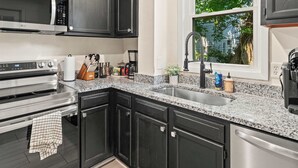 A modern kitchen with dark cabinets, stainless steel appliances, granite countertops, and a window with a view of greenery.