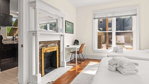 A bedroom with a fireplace, a desk, a chair, a bed with towels, and a view of the outside.