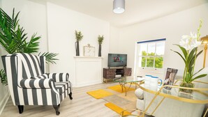 A modern living room with a striped armchair, a glass coffee table, and a television. - The Residence by Guestz (Cheltenham)