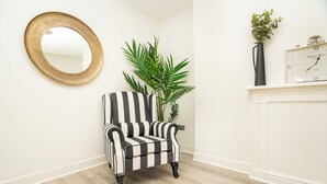 A room with a striped armchair, a round mirror, a potted plant, a clock, and a fireplace. - The Residence by Guestz (Cheltenham)