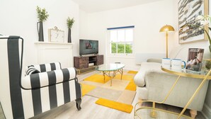 A modern living room with striped furniture, a glass coffee table, a television, and a window with a view. - The Residence by Guestz (Cheltenham)