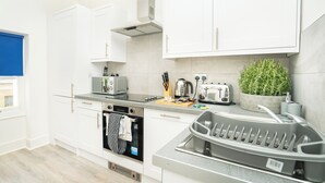A modern kitchen with white cabinets, a built-in oven, a toaster, and a coffee maker. - The Residence by Guestz (Cheltenham)