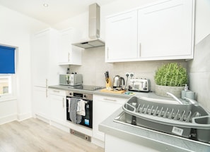 A modern kitchen with white cabinets, a built-in oven, a toaster, and a coffee maker. - The Residence by Guestz (Cheltenham)