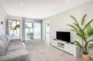 Ein modernes Wohnzimmer mit einer Couch, einem Fernseher auf einer weißen Unterhaltungseinheit und einer großen Topfpflanze.
