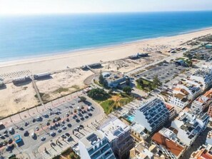 Luftaufnahme einer Küstenregion mit Strand, Parkplatz und Wohngebäuden.