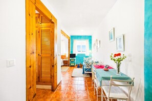 A hallway leading to a room with a window, a table with chairs, and a vase with flowers. - Portón 3 Studio – Perfect for Couples (Conil de la Frontera)