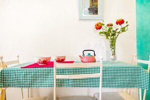 A dining table with a green and white checkered tablecloth, a pink teapot, two bowls, and a vase with flowers. - Portón 3 Studio – Perfect for Couples (Conil de la Frontera)