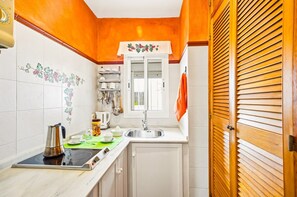 A compact kitchen with a stove, sink, and cabinets, a window with a view, and a wooden door. - Portón 3 Studio – Perfect for Couples (Conil de la Frontera)