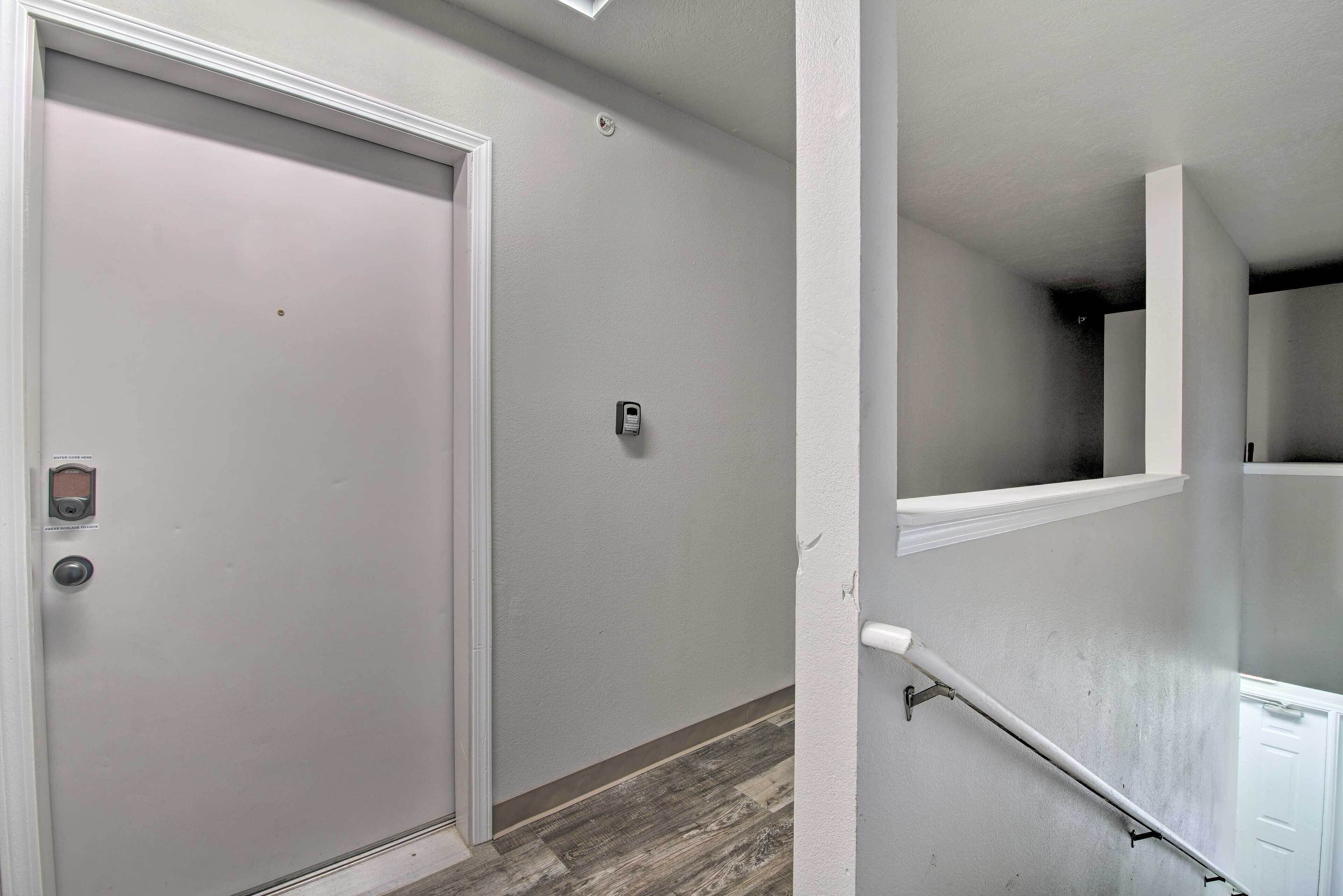 Un pasillo con una puerta cerrada, un portero automático en la pared y una barandilla que lleva a un rellano.