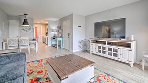 Een woonkamer met een televisie, een houten salontafel, een eethoek met stoelen en een keuken op de achtergrond.