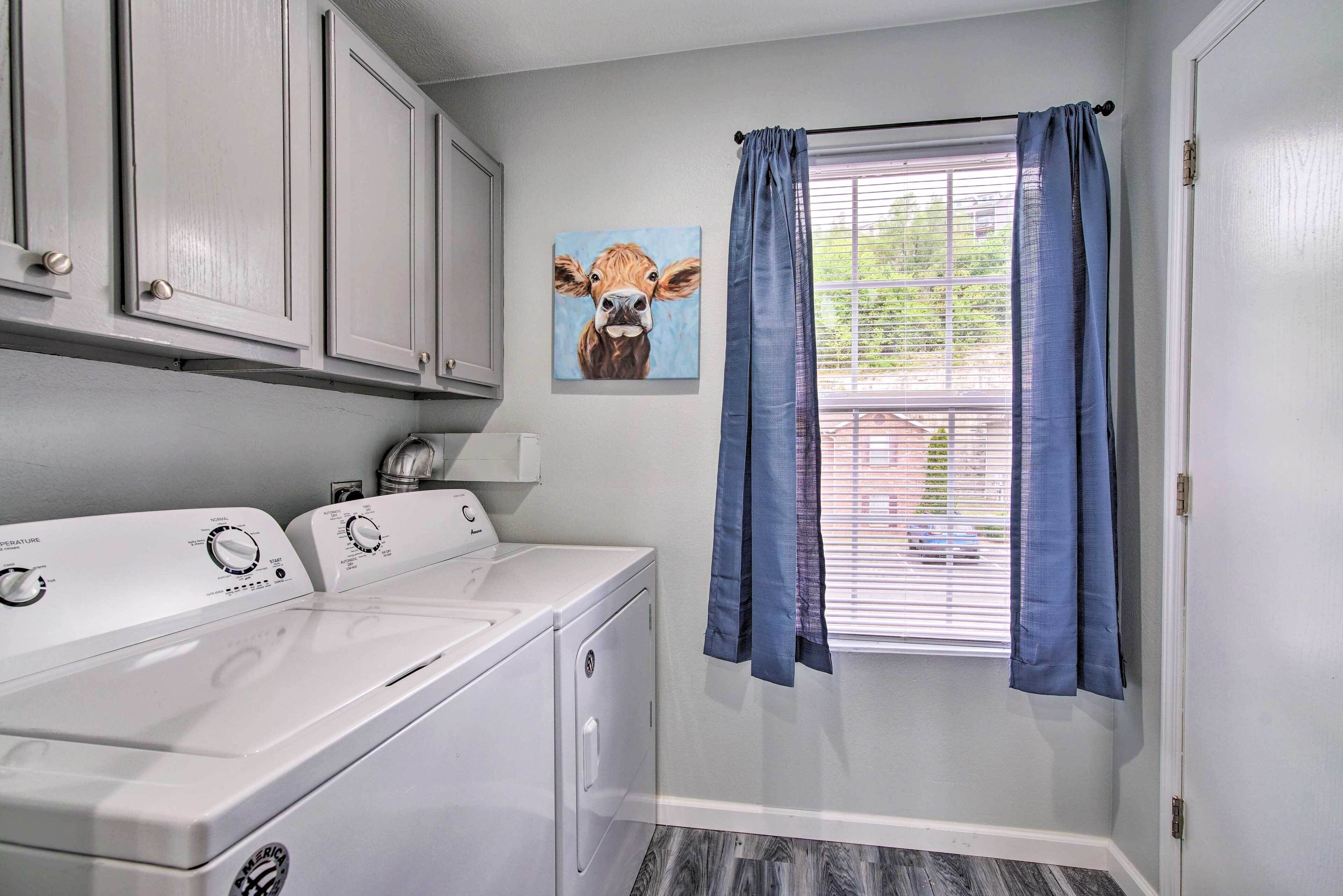 A laundry room with a front-loading washer and dryer, a window with blue curtains, and a wall-mounted drying rack.