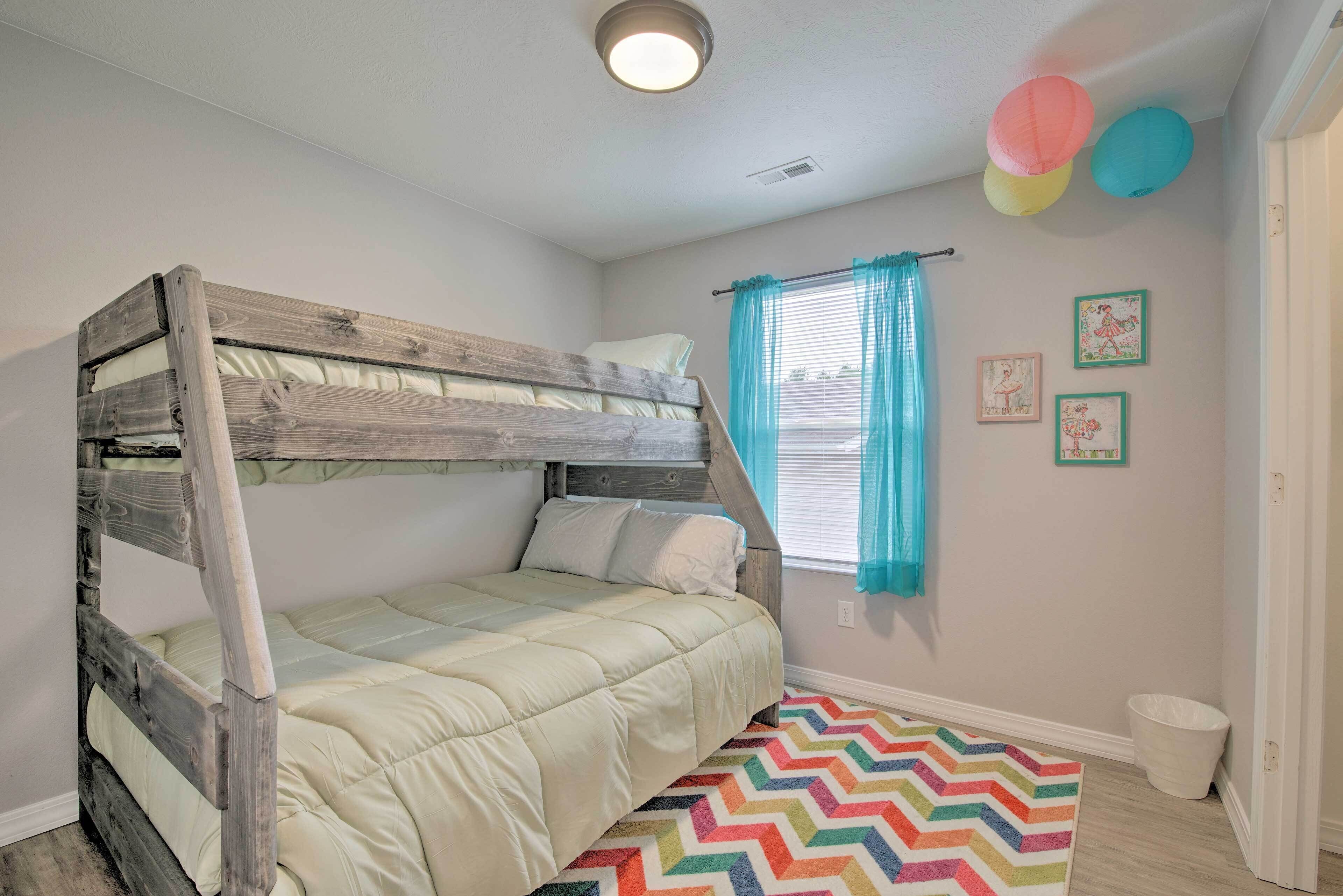A bunk bed with a wooden frame and a quilted mattress, a window with blue curtains, and a colorful chevron-patterned rug.